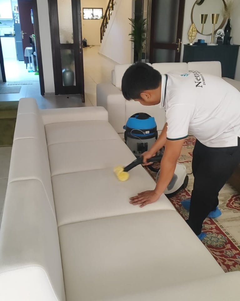 Man cleaning white upholstered furniture with a handheld cleaning machine in an indoor space