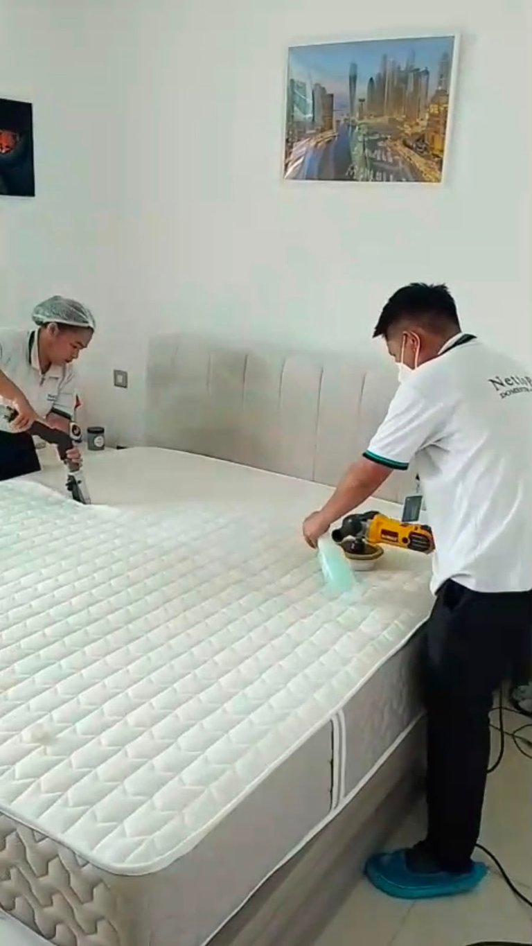 Two workers inspecting a mattress in a bedroom, one holding a device for testing quality