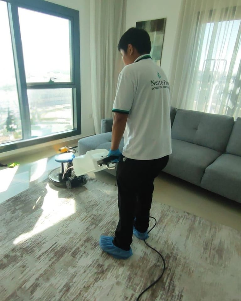 Worker polishing apartment floor with machine while standing in modern living room with windows and gray sofa