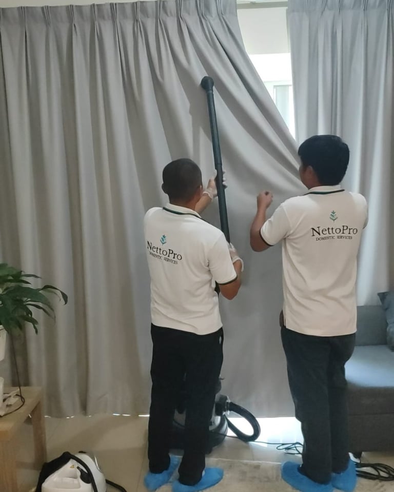 Two NettoPro workers in beige shirts cleaning gray curtains with a pole tool in a modern room
